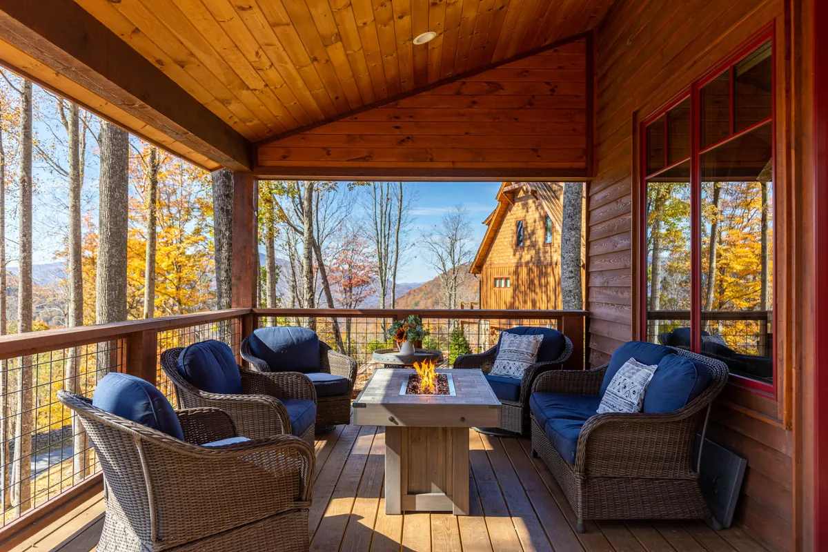 A cozy fire pit surrounded by comfortable seating beneath sturdy wooden beams. The setting overlooks a scenic mountain view, with the warm glow of the firepit inviting guests to gather, relax, and enjoy the outdoors at sunset or after dark.