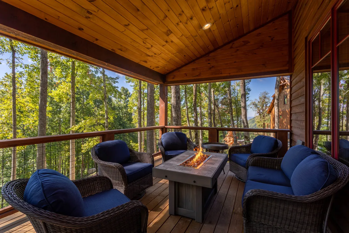 A welcoming outdoor fire pit area framed by comfortable seating and rustic wooden beams, nestled among trees. The natural surroundings and flickering fire create an intimate, romantic ambiance for evening gatherings or quiet reflection.
